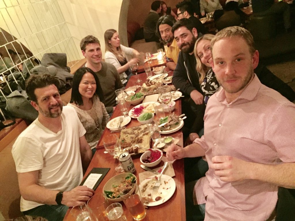 Photo os 8 people sitting at a long rectangular table having dinner. a few Kanopians are in the photos. 