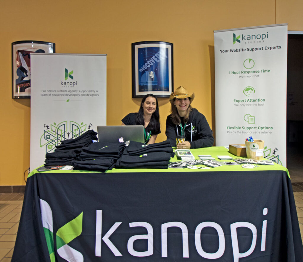 Two women, one wearing a cowboy hat, sitting at a conference booth with signs that say Kanopi Studios