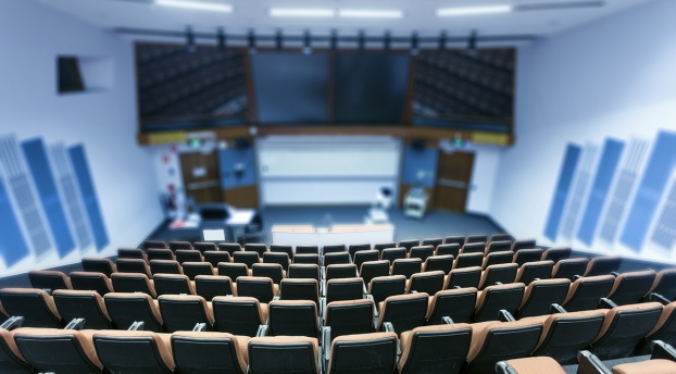 A large classroom in a higher education setting: there are many seats facing a large video screen and dry-erase board. 