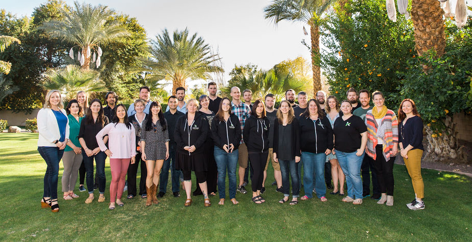 Kanopi staff in casual clothes standing in a group and smiling, outside with palm trees. 