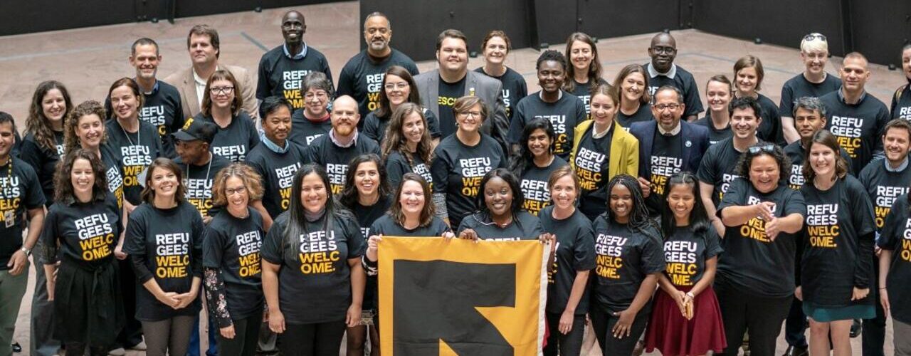 Large group of about 40 people in IRC tshirts smiling at the camera. The people in the center are holding a large banner with the IRC logo