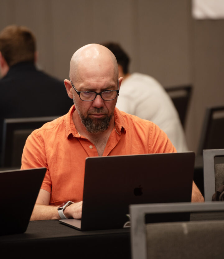 A Kanopian in orange shirt wearing glasses working at his laptop