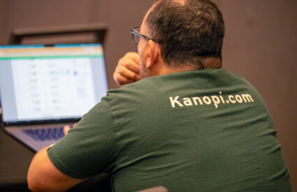 Kanopian from the back looking at a laptop. Their tshirt says kanopi.com on the back.