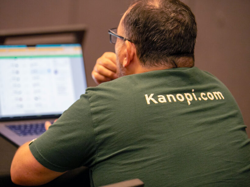 Kanopian from the back looking at a laptop. Their tshirt says kanopi.com on the back.