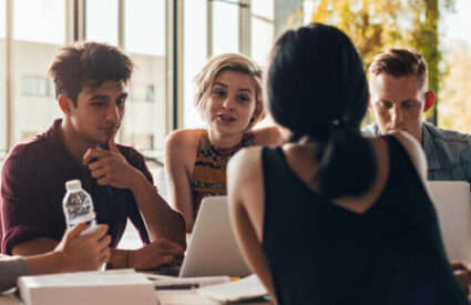 Four students study at a table with laptops and notebooks