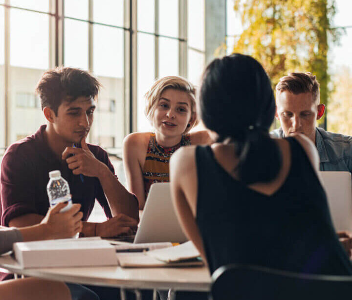 Four students study at a table with laptops and notebooks