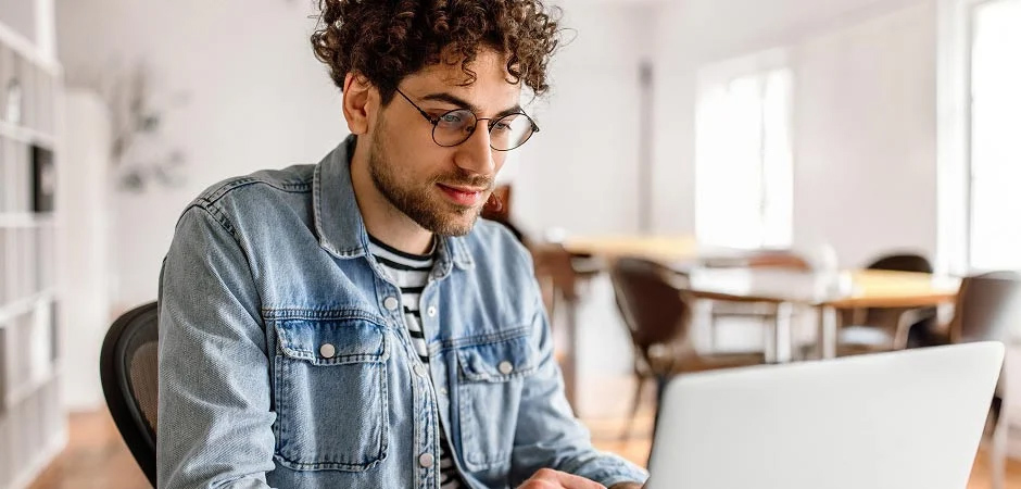 Man with glasses and a denim shirt looking at his laptop