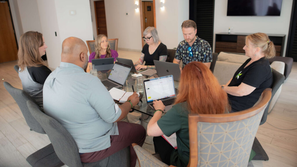The seven members of the Kanopi leadership team sit around a table with their laptops