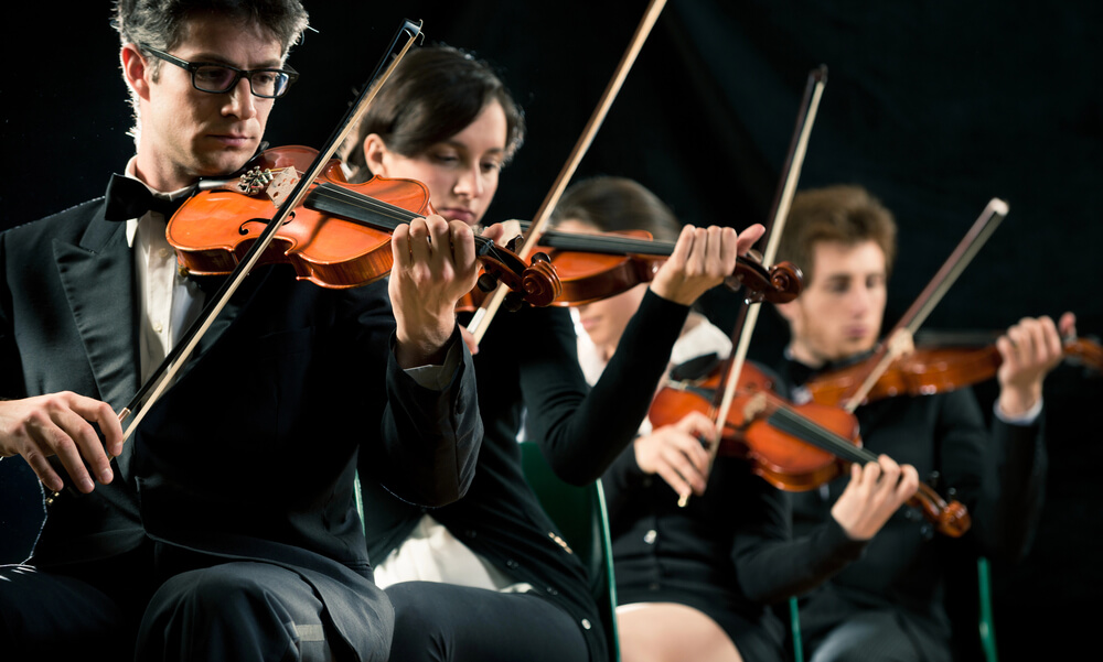 Four violinists play while seated, wearing dark suits