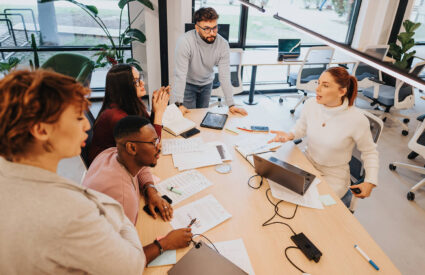 A diverse group of marketing professionals meets at a large conference table to discuss strategy