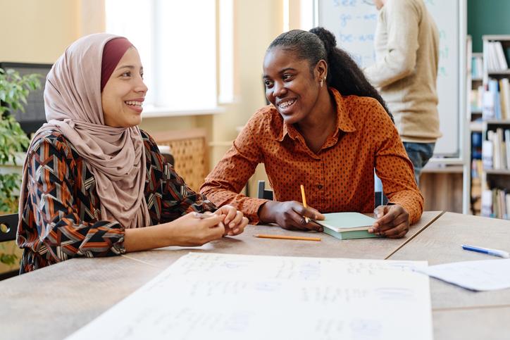 Two women sitting at a table smiling as they fill out paperwork
